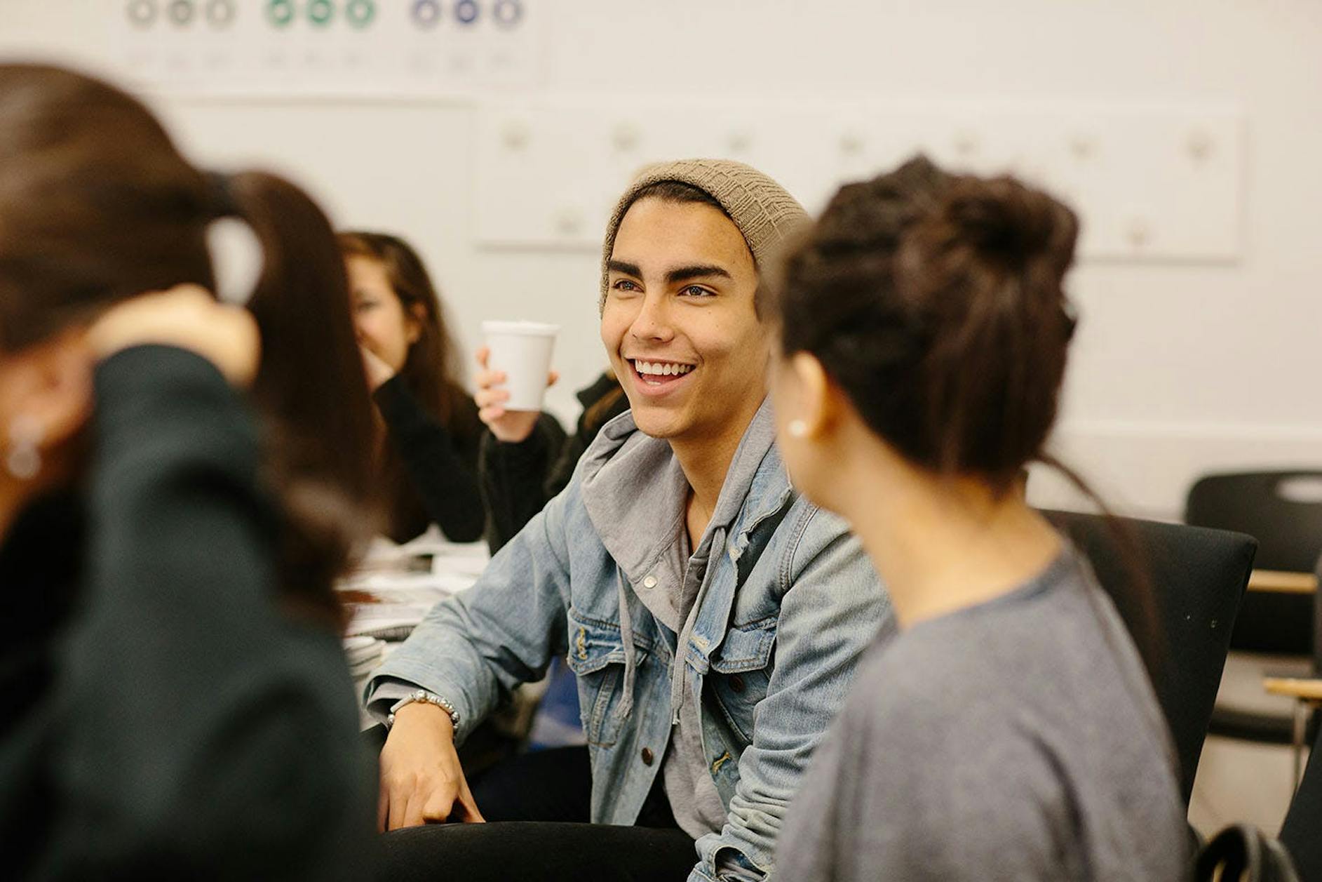 A student smiles while talking to another student in a classroom.