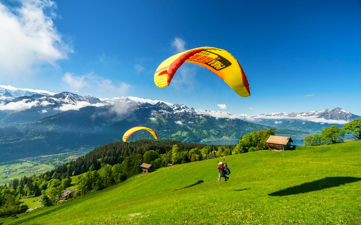 Paragliders soaring over Interlaken, Switzerland, with views of mountains and Lake Thun.