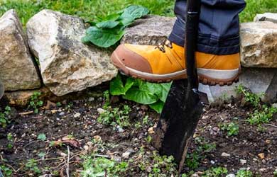 Yellow boot pushing spade into some soil
