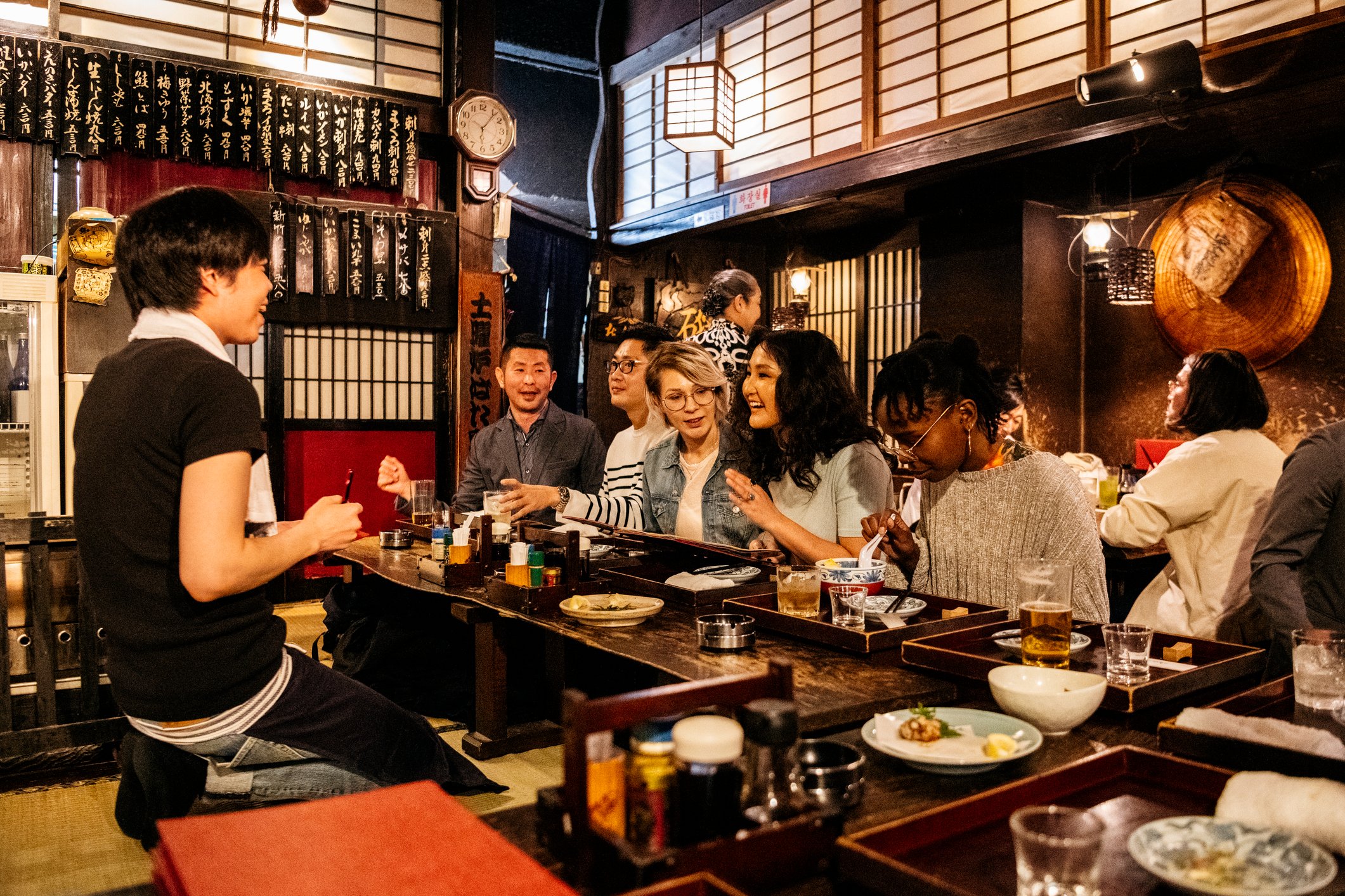 Waiter taking food order from happy group of friends, night out, drinking, eating in Tokyo, Japan.