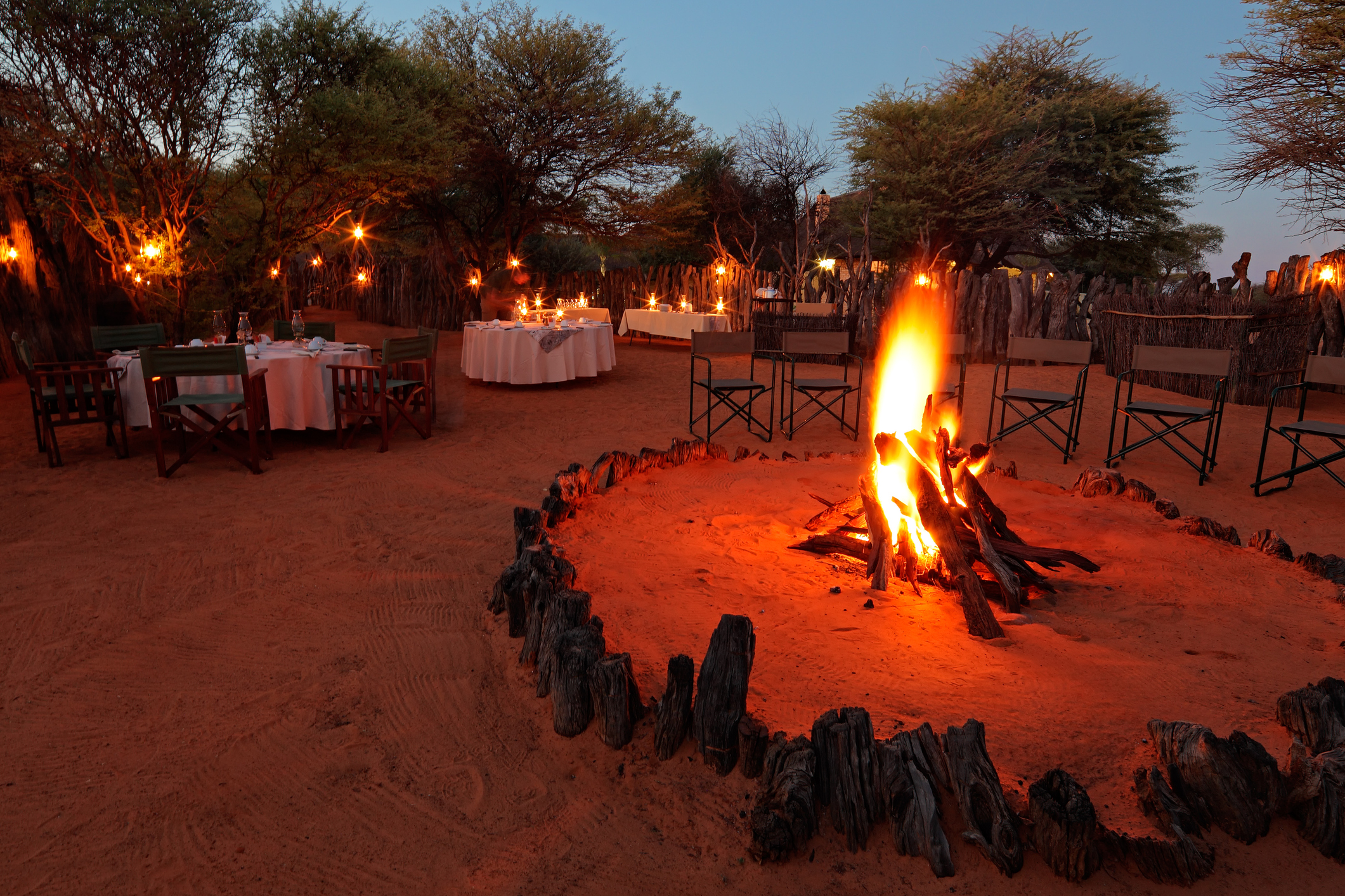 Nighttime campfire and decorated tables for outdoor safari Boma dinner in South Africa.