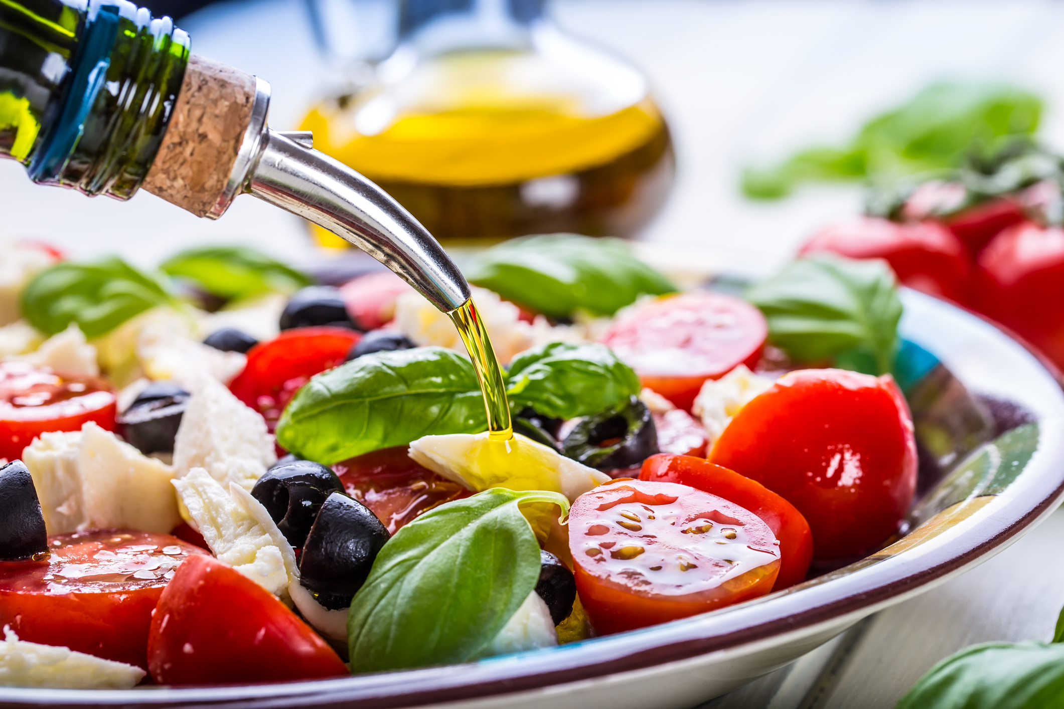 Someone pouring olive oil over a fresh and dlelicious looking caprese salad in Italy.