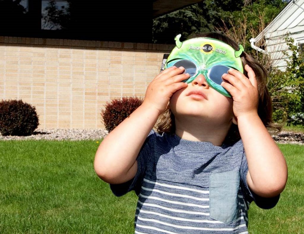 A child is shown with protective viewing glasses during a solar eclipse.