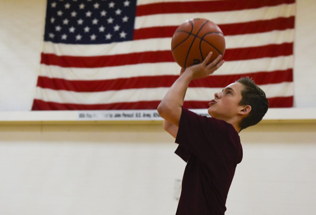Hit the Mitt helps kids like Parker Teff, a 14-year-old who was born with cerebral palsy and stays loose and healthy playing on three Gold Crown Foundation teams. Here Parker takes a shot with an American flag behind him. Photo by Cyrus McCrimmon.