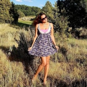Louisa Drouet poses in a meadow. She's wearing a light dress with pine trees behind her.
