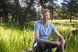Jonathan Proctor sits on a rock in a meadow. He is the Rockies and Plains program director for Defenders of Wildlife and enjoys the outdoors.