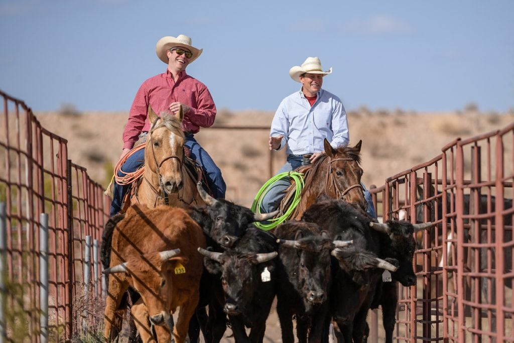 Dr. Jason Stoneback, left, is on his horse riding through a corral next to his patient, Archie Chant, who is also on his horse. They're riding side-by-side.