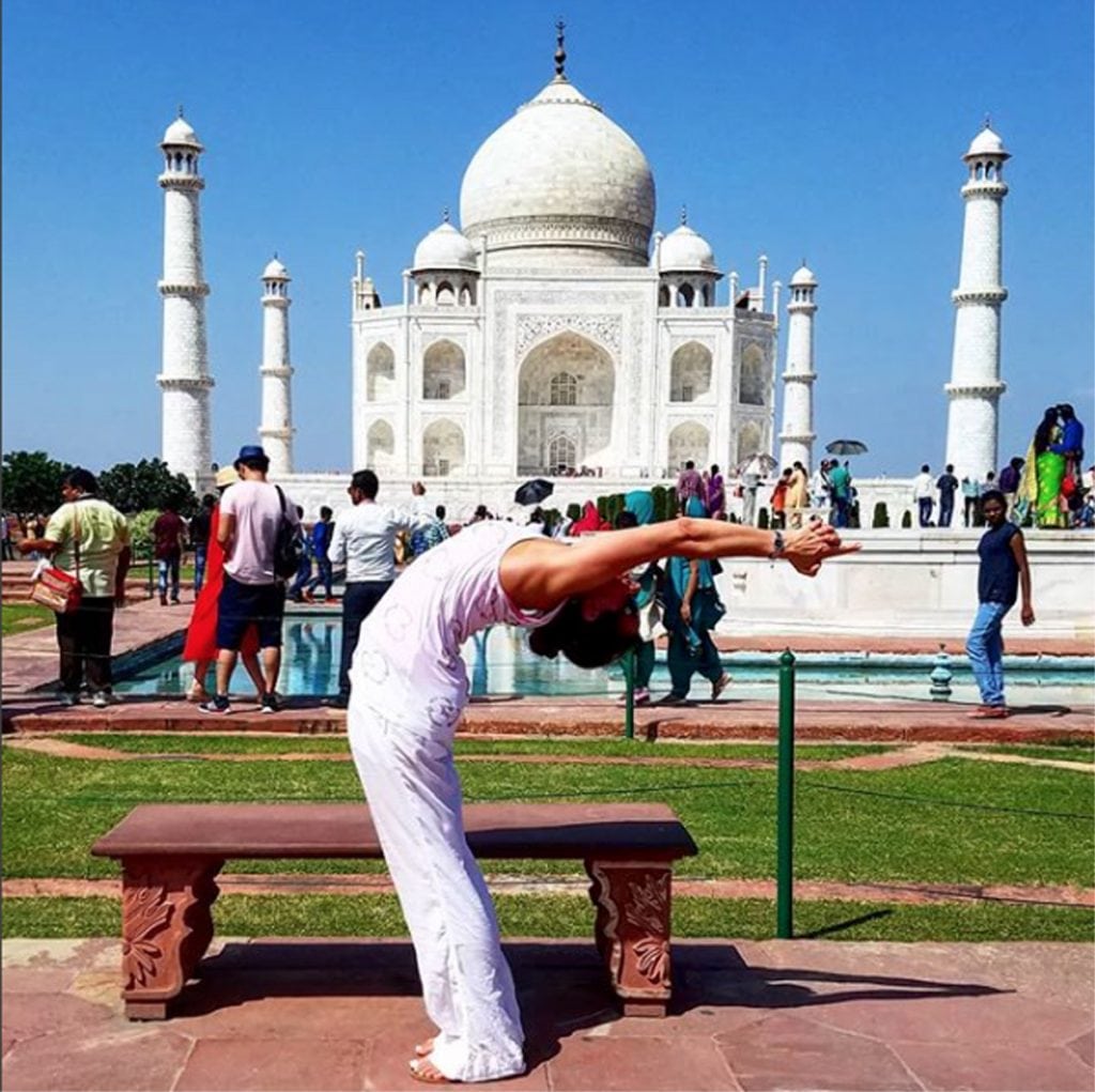 A woman wearing white does a yoga pose in front of the Taj Mahal in India.