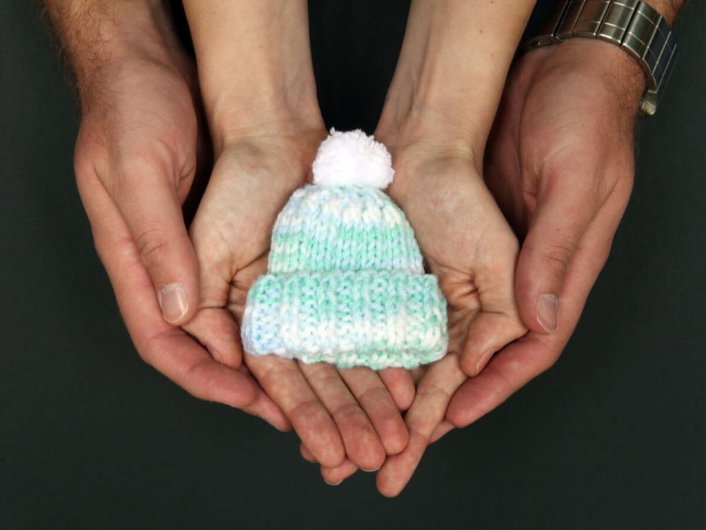 Parents hold a blue baby hat.