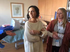 a woman stands in a labor and delivery room at University of Colorado Hospital. In the background is a cooling bassinet called a Cuddle Cot.