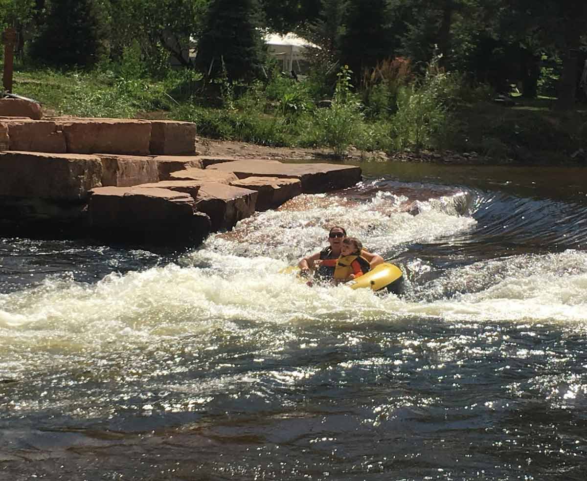 woman and child going down a rapid in Colorado summer tubing river.