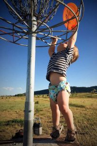 toddler stretching up to put a disc into the basket at a course in Fort Collins.