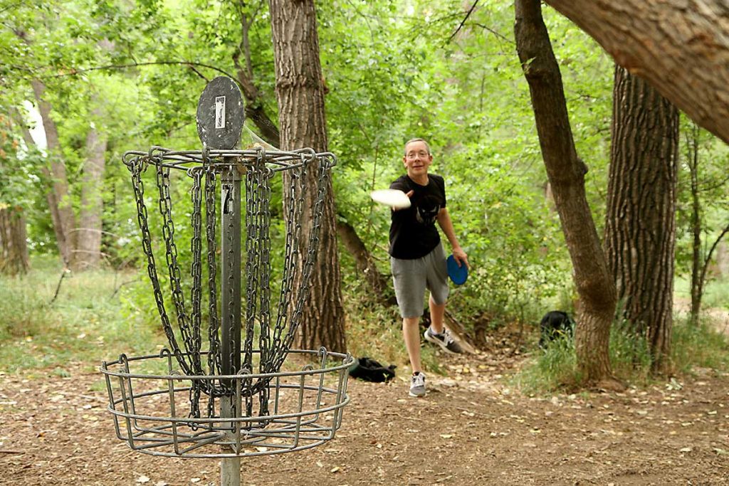man tosses disc at disc golf basket