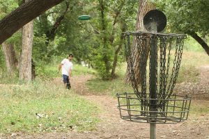 man tosses disc at disc golf basket