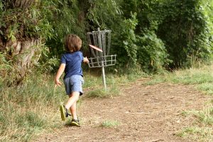 4-year-old puts his disc into the basket at one of the great disc golf courses in Colorado.