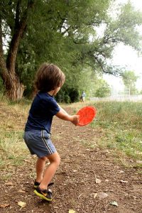 4-year-old boy gets ready to toss a disc at a basket while his father watches one of the great disc golf courses in Colorado.