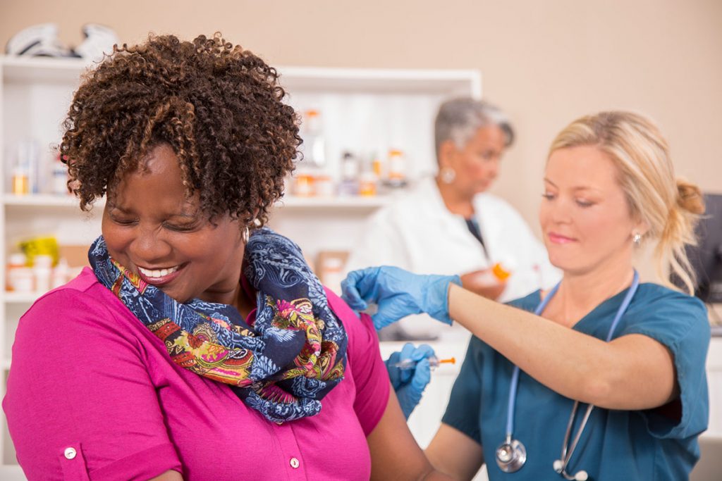 A nurse gives a woman a flu shot as she turns away and cringes
