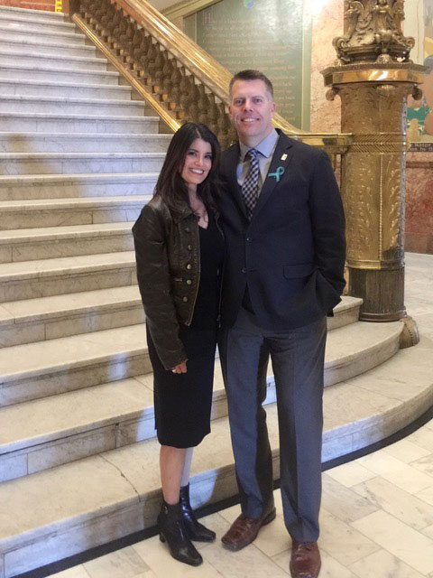 Angela with her husband in front of a hotel staircase.