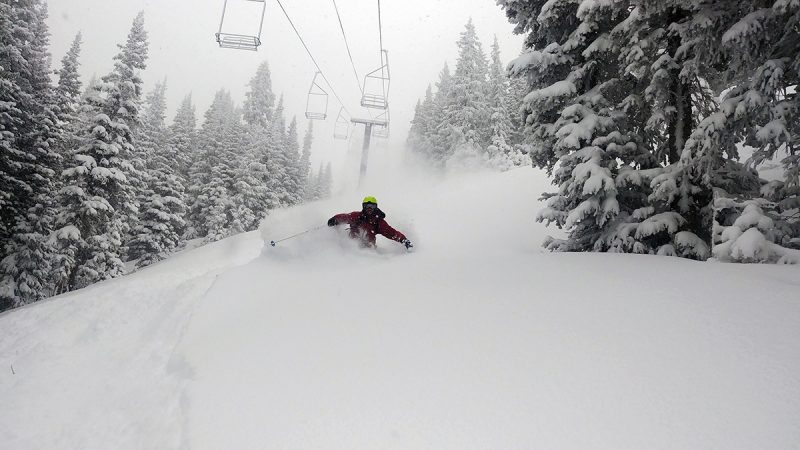 In this photo, a skier skis under a lift in chest-deep snow.