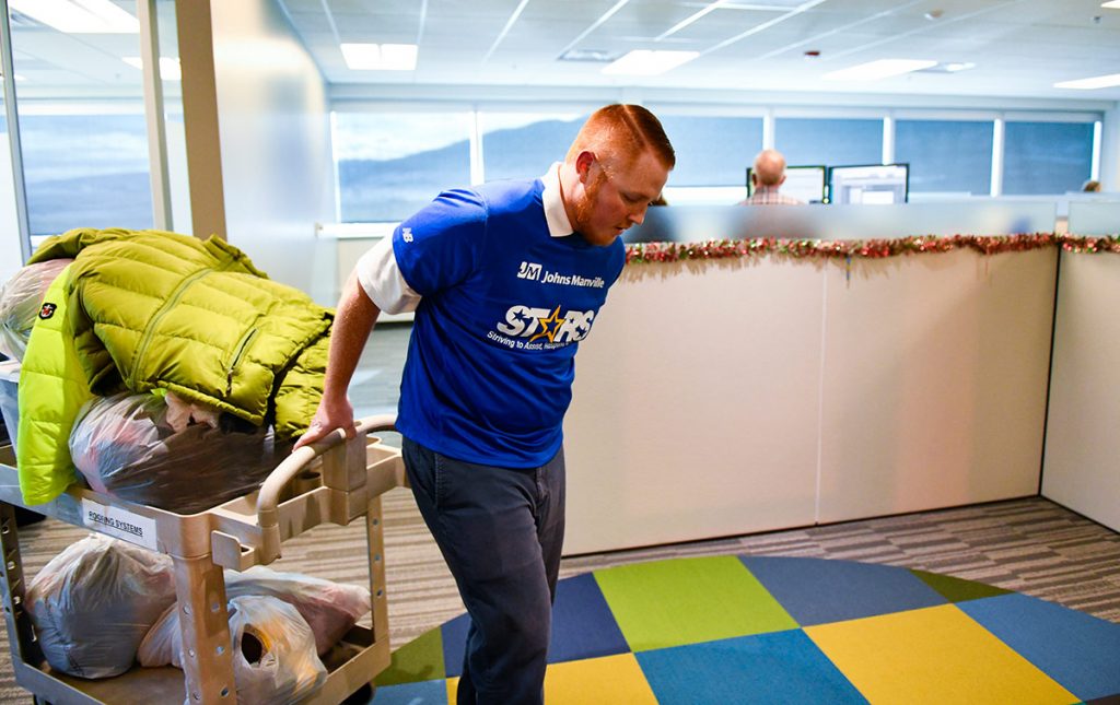Frostbite survivor, Alec Grimes, carries a bunch of coats, socks and gloves to his desk for his warm gear drive.