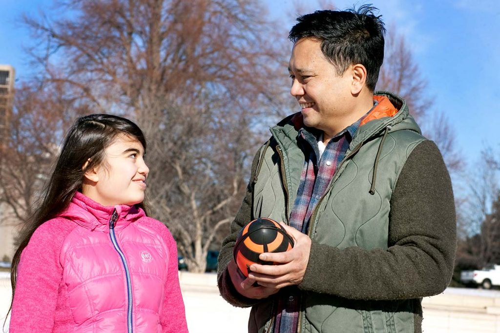 dad holds football while smiling at his teenage daughter.