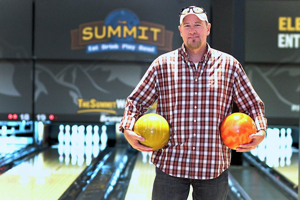 keith stands holding two bowling balls in front of the bowling lane.