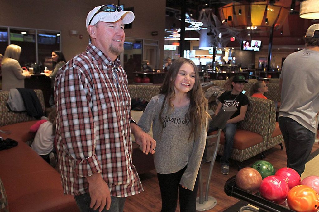 daughter holds her dads hand at a bowling alley.