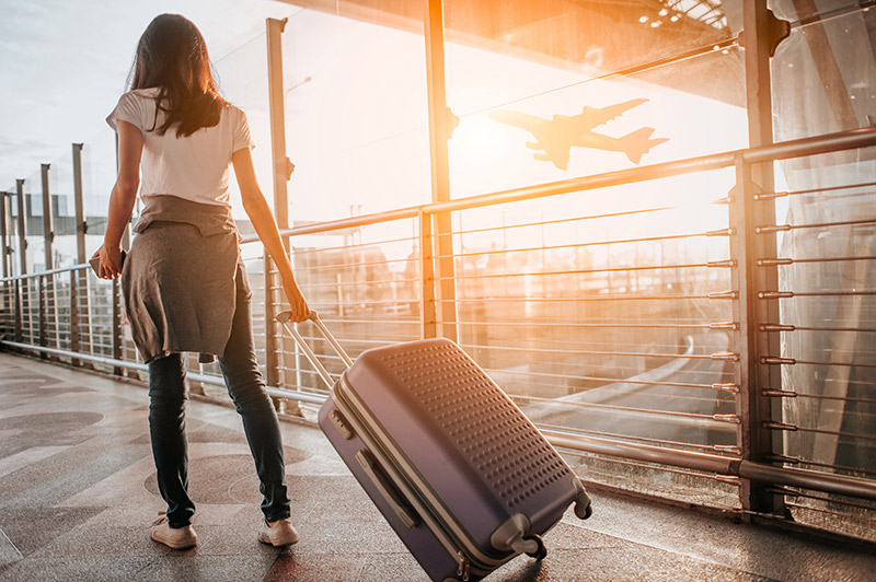 Travel plans and coronavirus - What should you do? A woman walks with her suitcase at an aiprort.