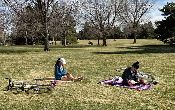 Women in Denver practice physical distancing. They are sitting about six feet apart in a park.