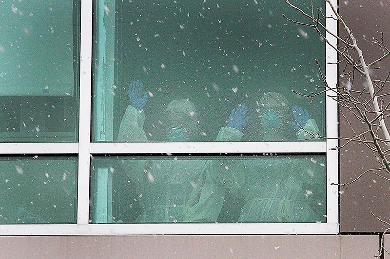 health care nurses in PPE wave thanks out the window of a hospital.