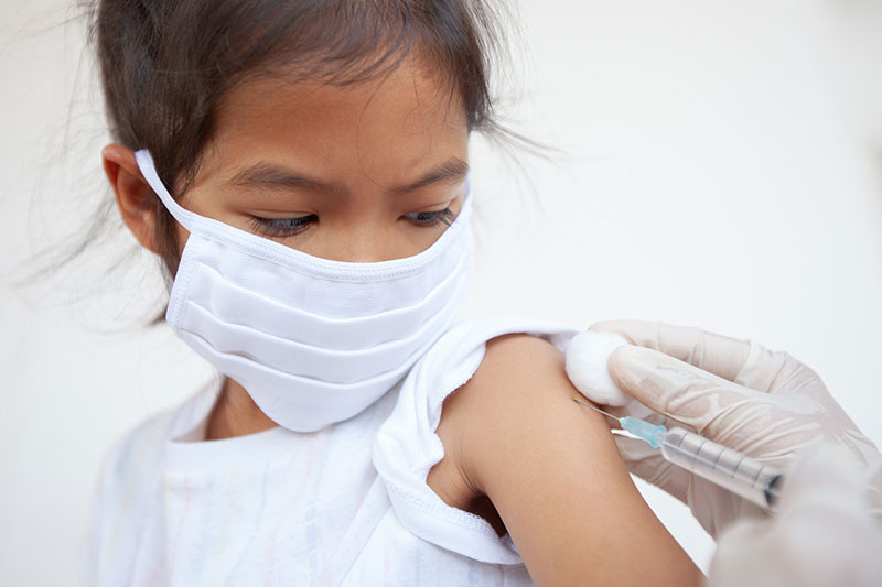 Child wearing a mask gets an child immunization during pandemic.