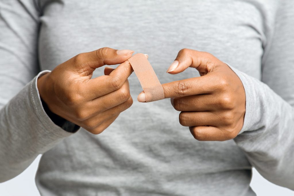 a woman wraps a Band-Aid around her finger to start the wound healing process.
