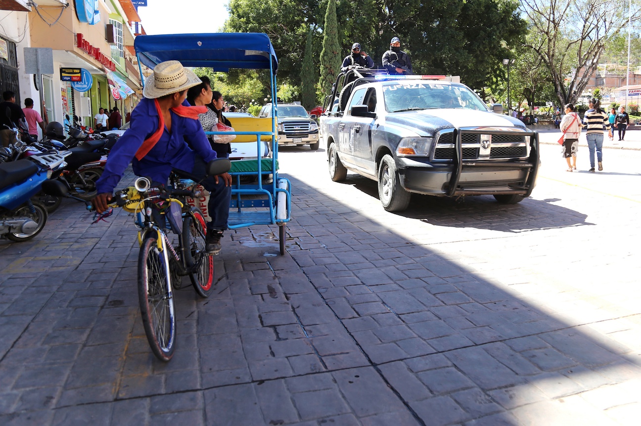 Un bicitaxista y sus pasajeros observan el paso de una patrulla de la Policía del estado en la ciudad Chilapa ante la ola de violencia que se vive en esta ciudad y por lo que maestros no han regresado a laborar. Foto: Jesús Eduardo Guerrero