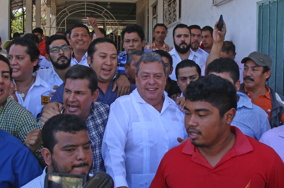 El ex gobernador, Ángel Aguirre Rivero sale protegido por sus simpatizantes, entre ellos el secretario estatal del PRD, Alberto Catalán, del salón de eventos sociales Ávila, donde padres de los 43 normalistas de Ayotzinapa desaparecidos exigieron una explicación sobre el paradero de sus hijos, durante el arranque de su precampaña a diputado federal en Ayutla. Foto: Carlos Alberto Carbajal