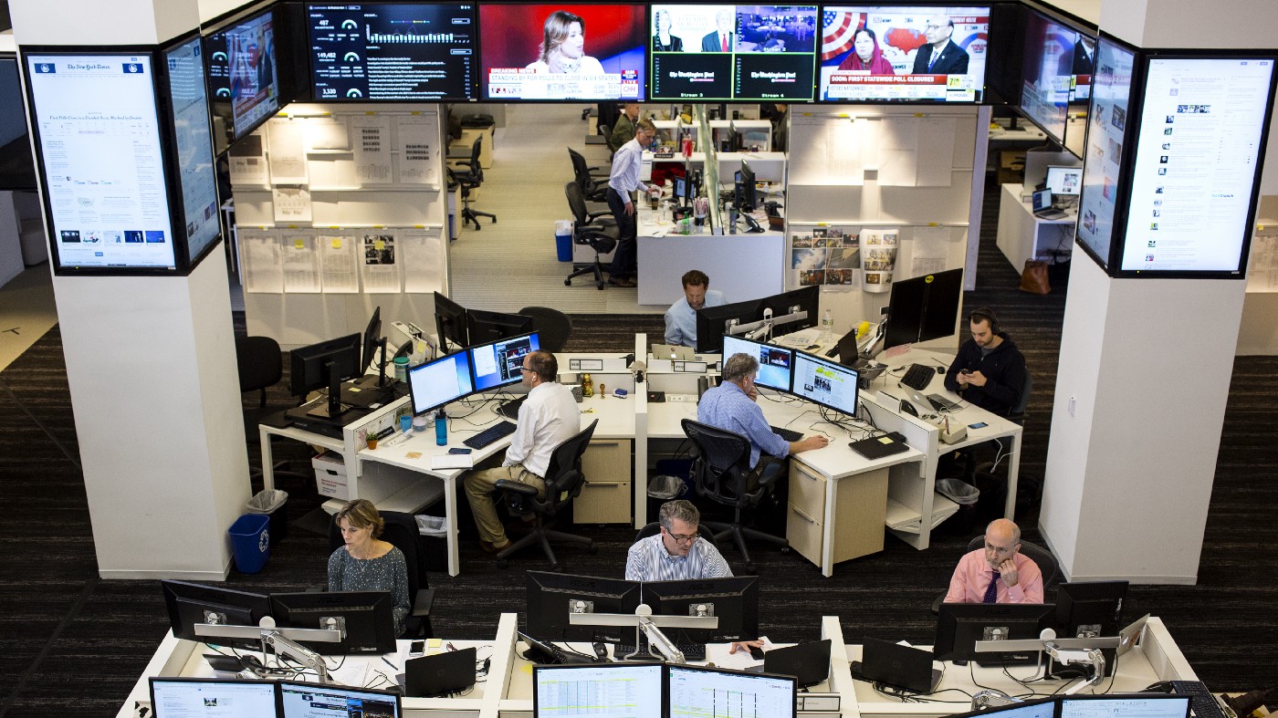 Washington Post'un haber odasından bir kare. Masalarında çalışan gazetecileri ve üstlerinde verilerin de olduğu ekranları gösteriyor.