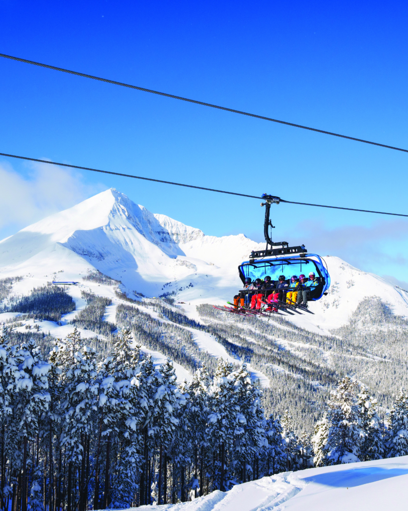 people on a ski lift with a clear blue sky and mountains in the background