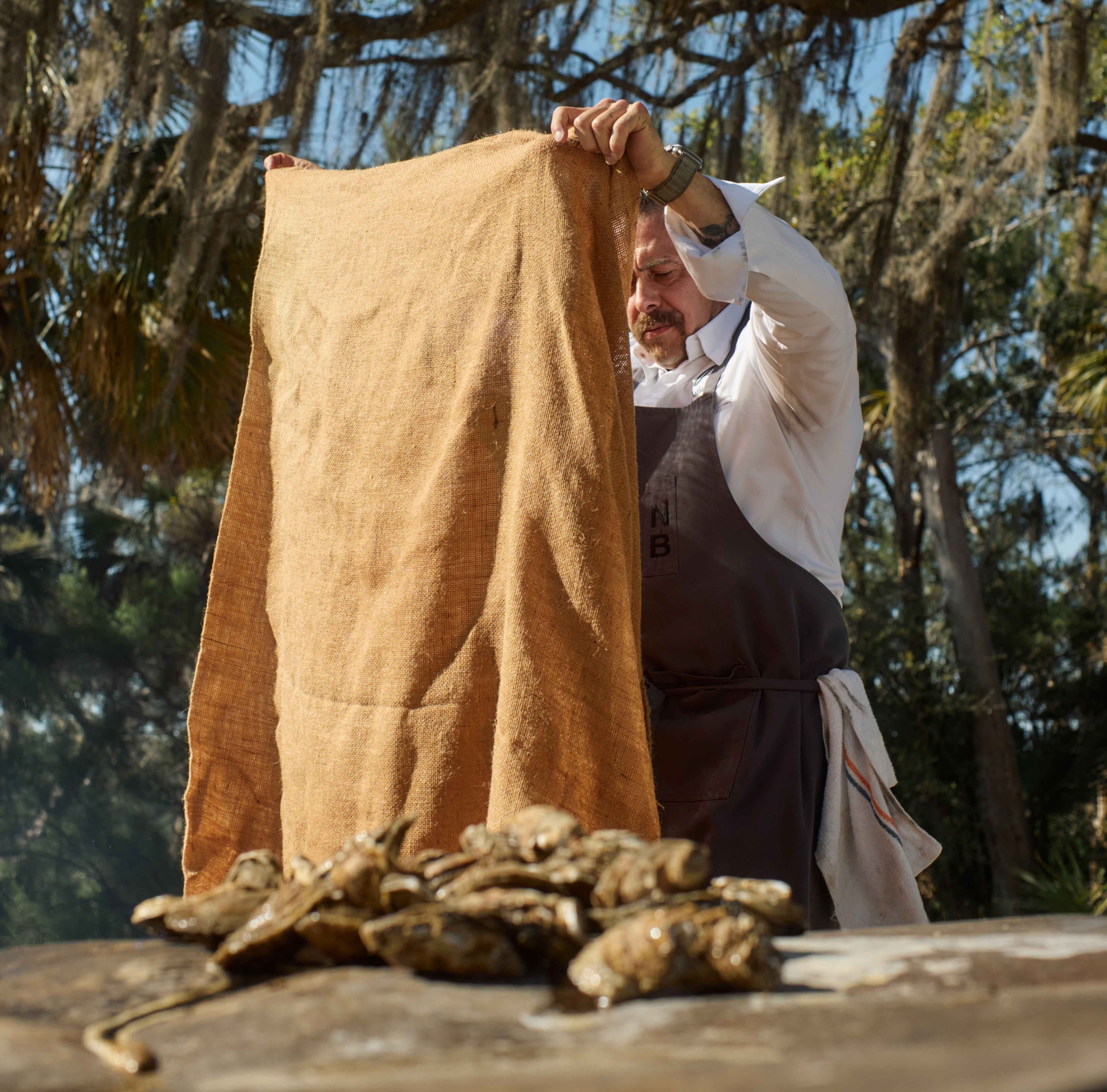 A man dumping oysters out of a burlap sack onto a table at Montage Palmetto Bluff oyster roast