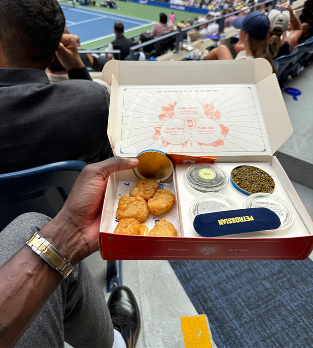 A person holding food in a box a the US Open