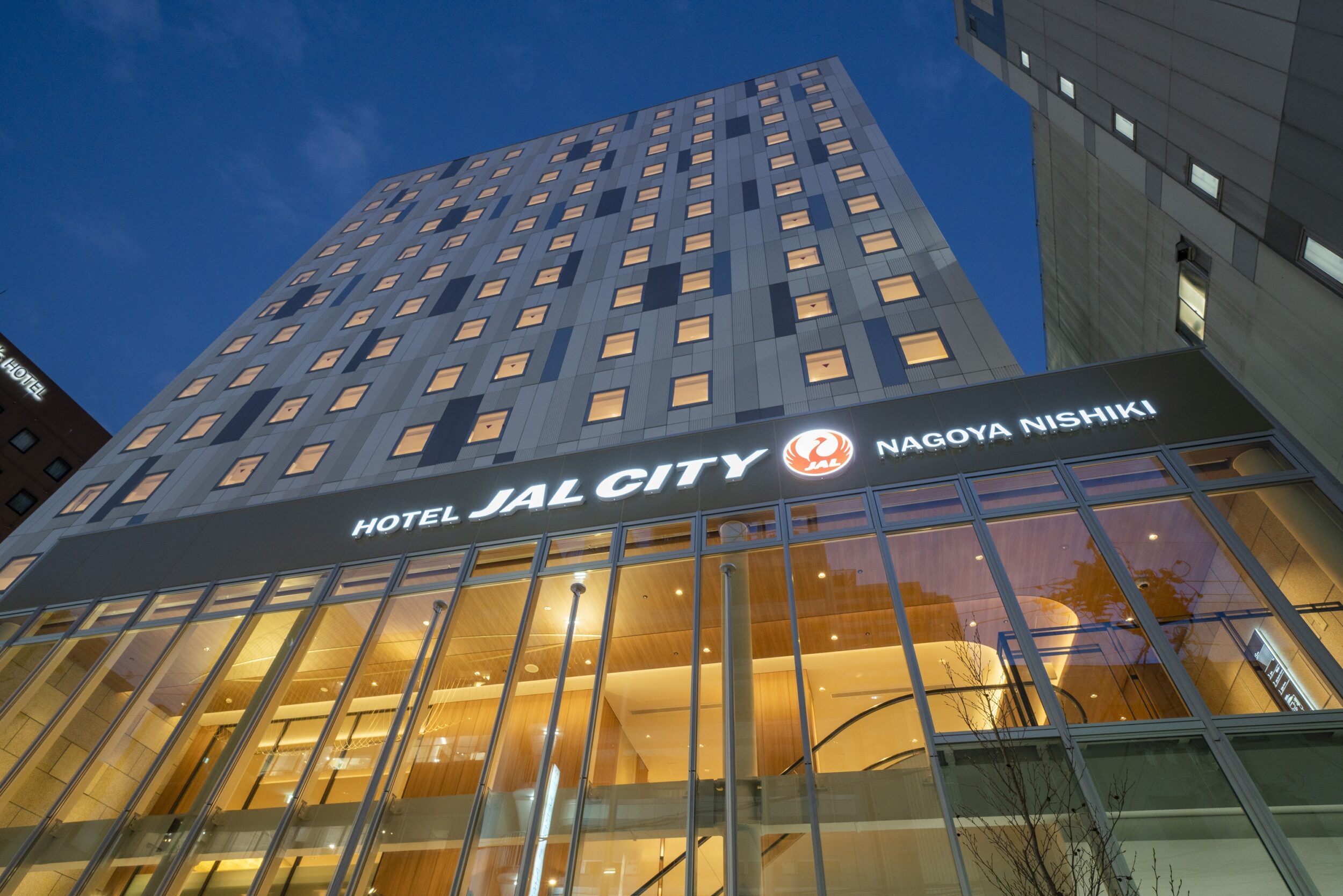 Exterior view of Hotel JAL City Nagoya Nishiki at dusk, with illuminated windows and a modern glass entrance.