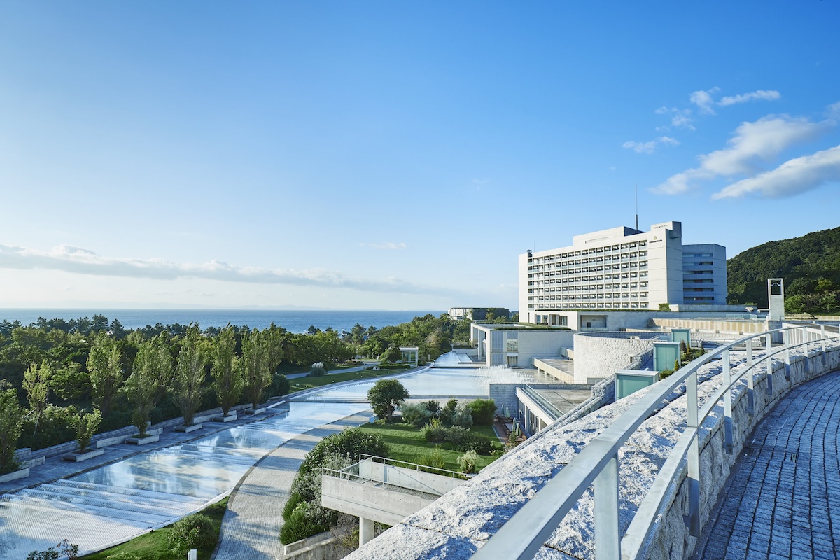 Grand Nikko Awaji, a modern coastal resort with tiered architecture, lush gardens, and ocean views under a bright blue sky.