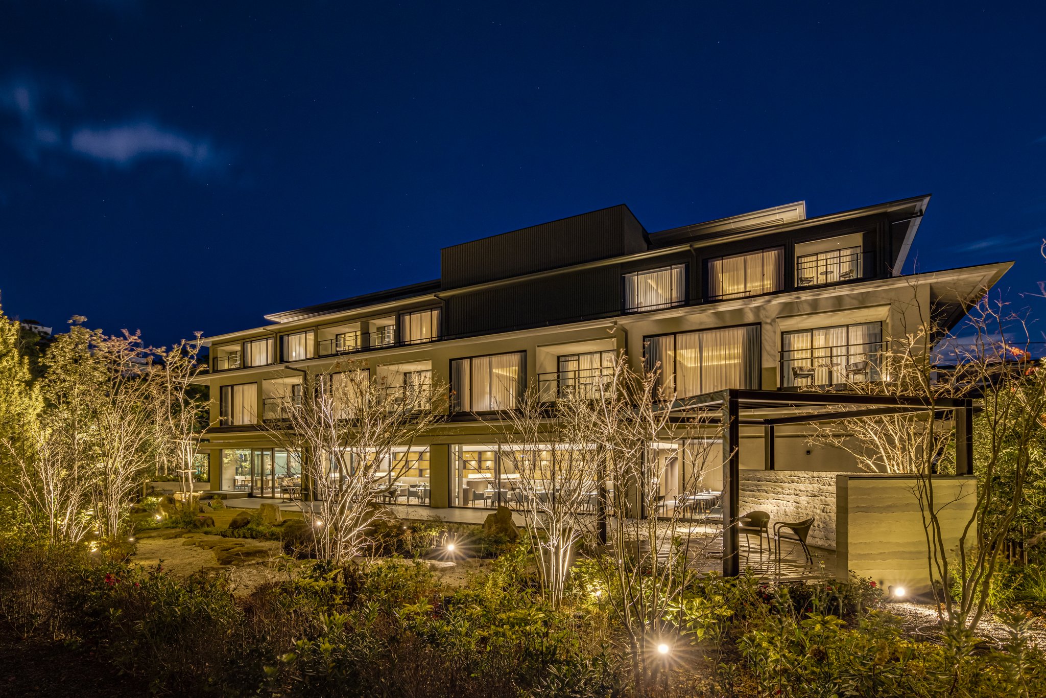 Hotel Okura Kyoto Okazaki Bettei, a low-rise luxury hotel warmly lit at night, surrounded by landscaped gardens and modern architecture.