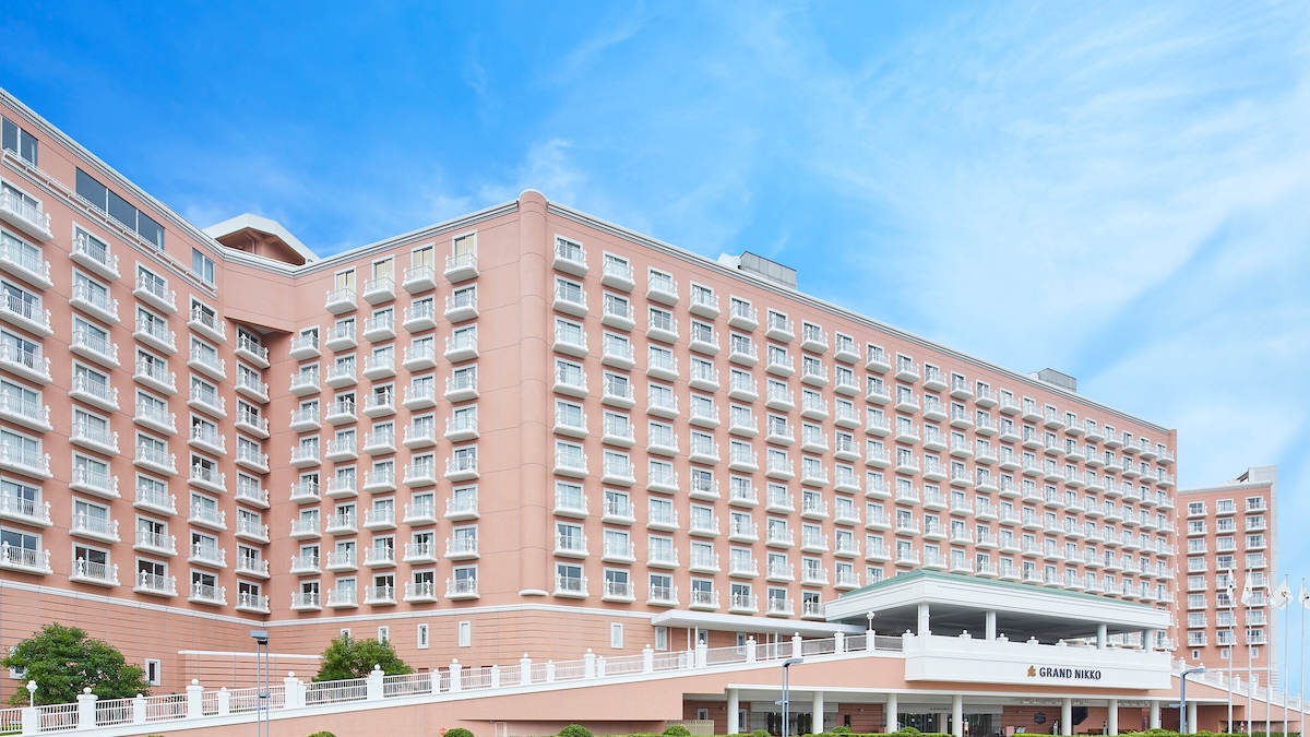 Grand Nikko Tokyo Bay Maihama, a large pink-hued hotel with white balconies and elegant architecture under a bright blue sky.