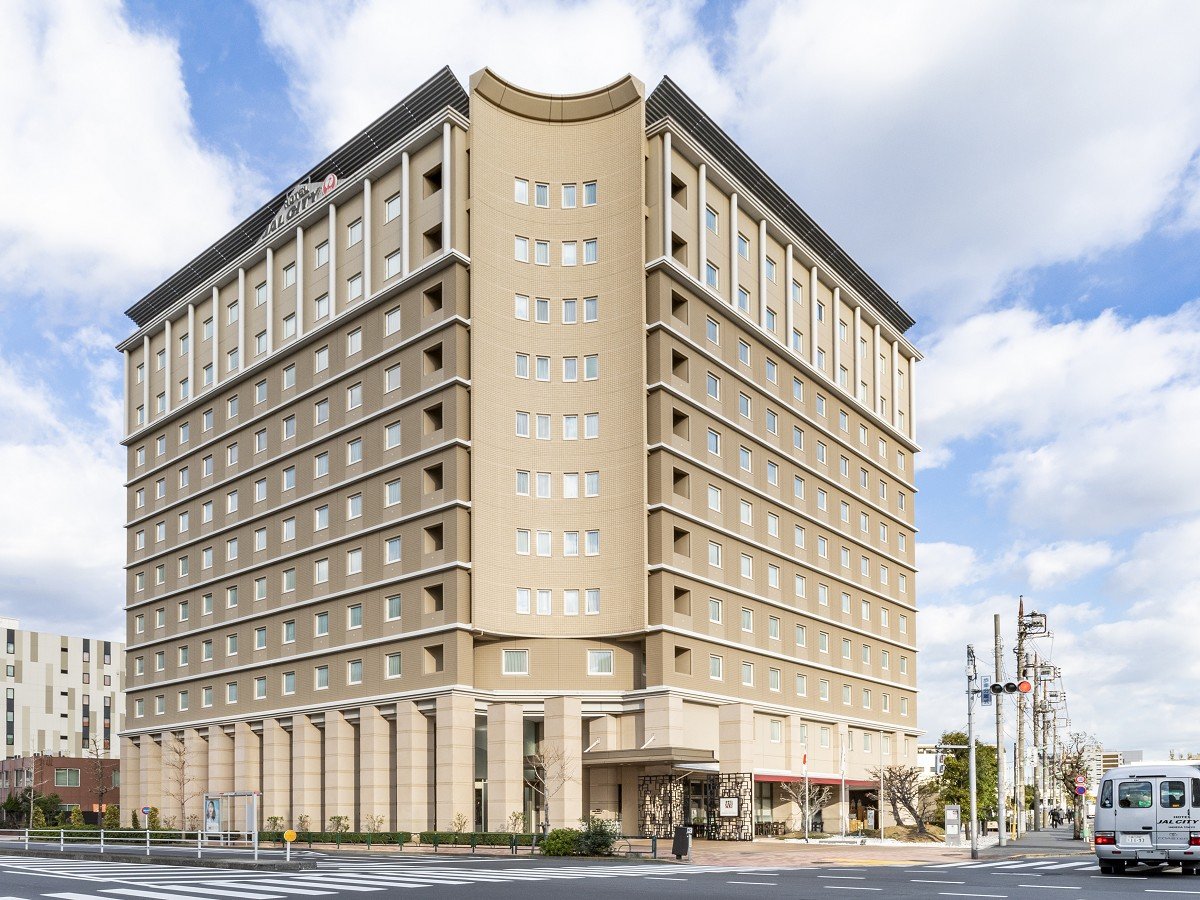 Hotel JAL City Haneda Tokyo, a beige mid-rise hotel with symmetrical windows on a city street under a partly cloudy sky.