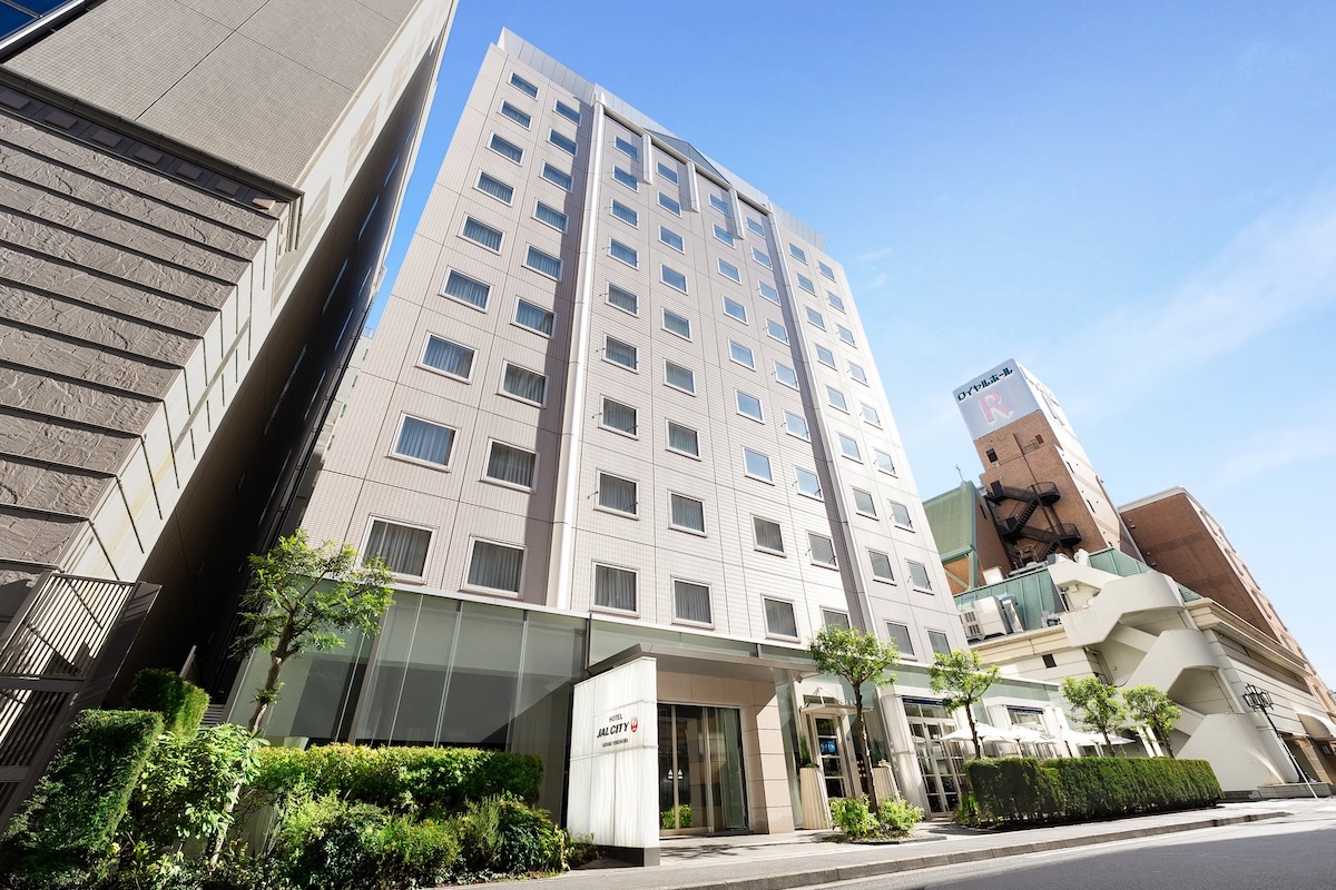 Hotel JAL City Kannai Yokohama, a modern high-rise hotel with clean lines and greenery at the entrance, set on a quiet city street under a clear sky.