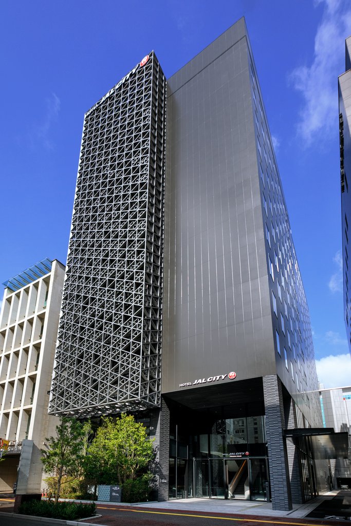 Hotel JAL City Fukuoka Tenjin, a sleek high-rise with a modern lattice facade and clean vertical lines under a clear blue sky.