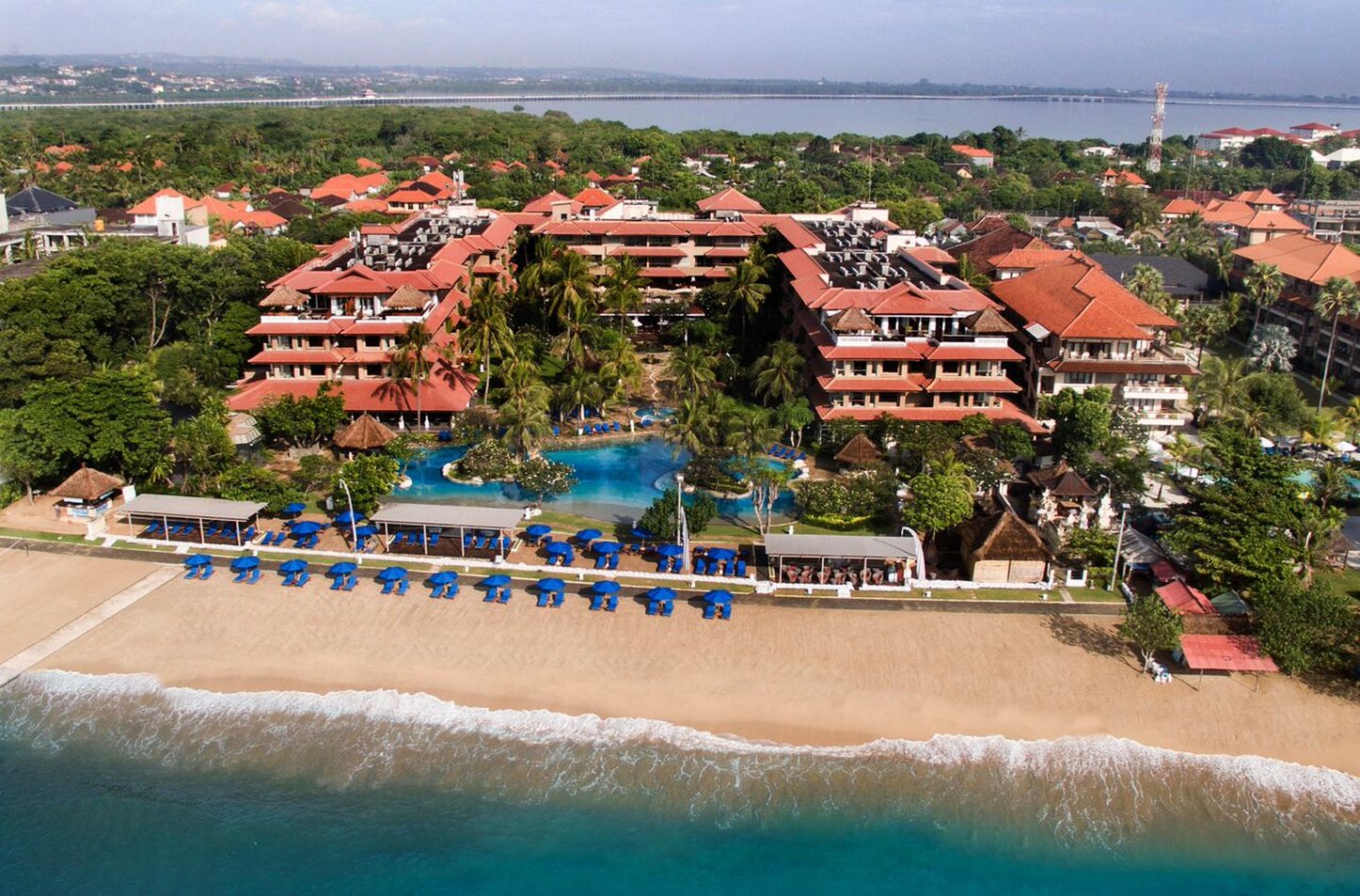 Hotel Nikko Bali Benoa Beach with beachfront access, blue umbrellas, and lush tropical surroundings.
