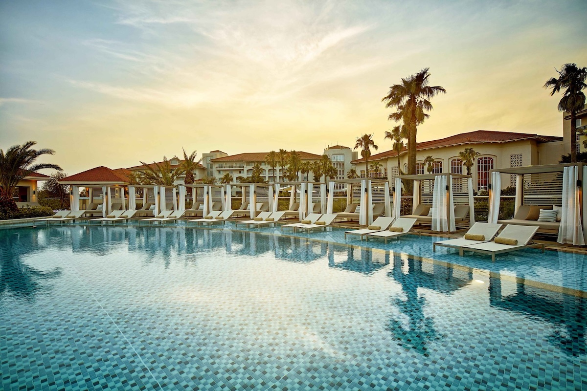 The Shilla Jeju resort with an inviting pool, cabana-style loungers, and palm trees at sunset.