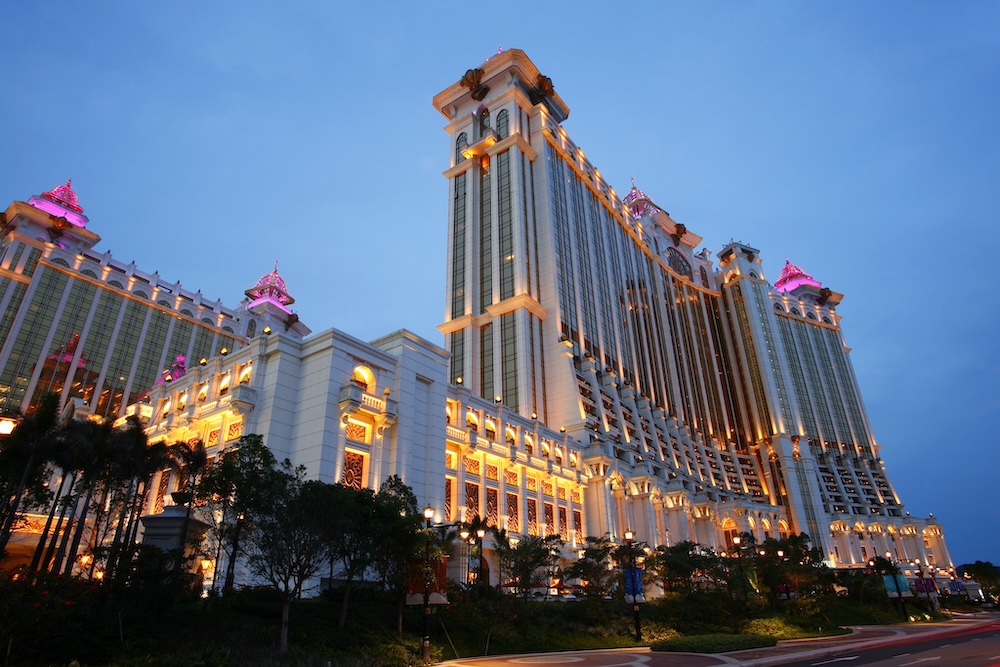 Hotel Okura Macau's illuminated tower and ornate façade glow under a vibrant twilight sky.