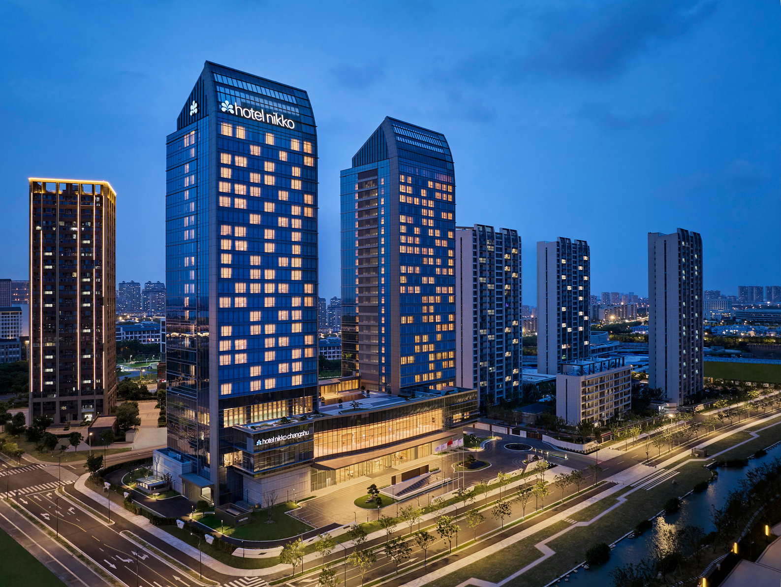 Hotel Nikko Changshu towers above a modern cityscape, its glass facade reflecting the twilight sky.