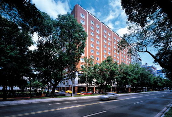 Hotel Royal-Nikko Taipei, a red-brick mid-rise building lined with trees, facing a wide urban road under a partly cloudy sky.